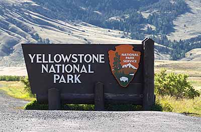 Wooden sign that reads "Yellowstone National Park" at the entrance to the park, with a mountain landscape in the background.